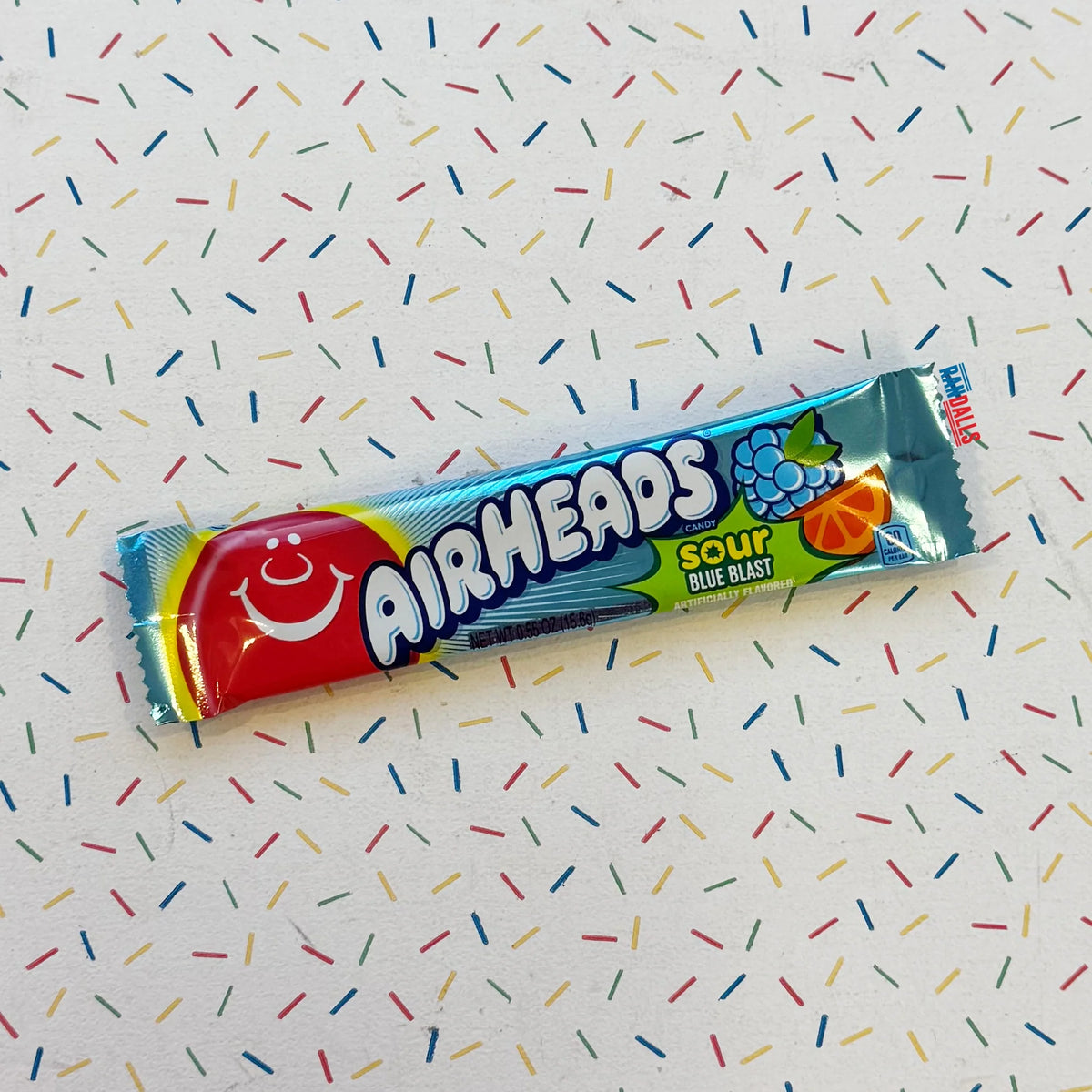 A single Airheads Sour Blue Blast candy stick in its original blue wrapper, placed diagonally on a white background with a colorful confetti sprinkle pattern.